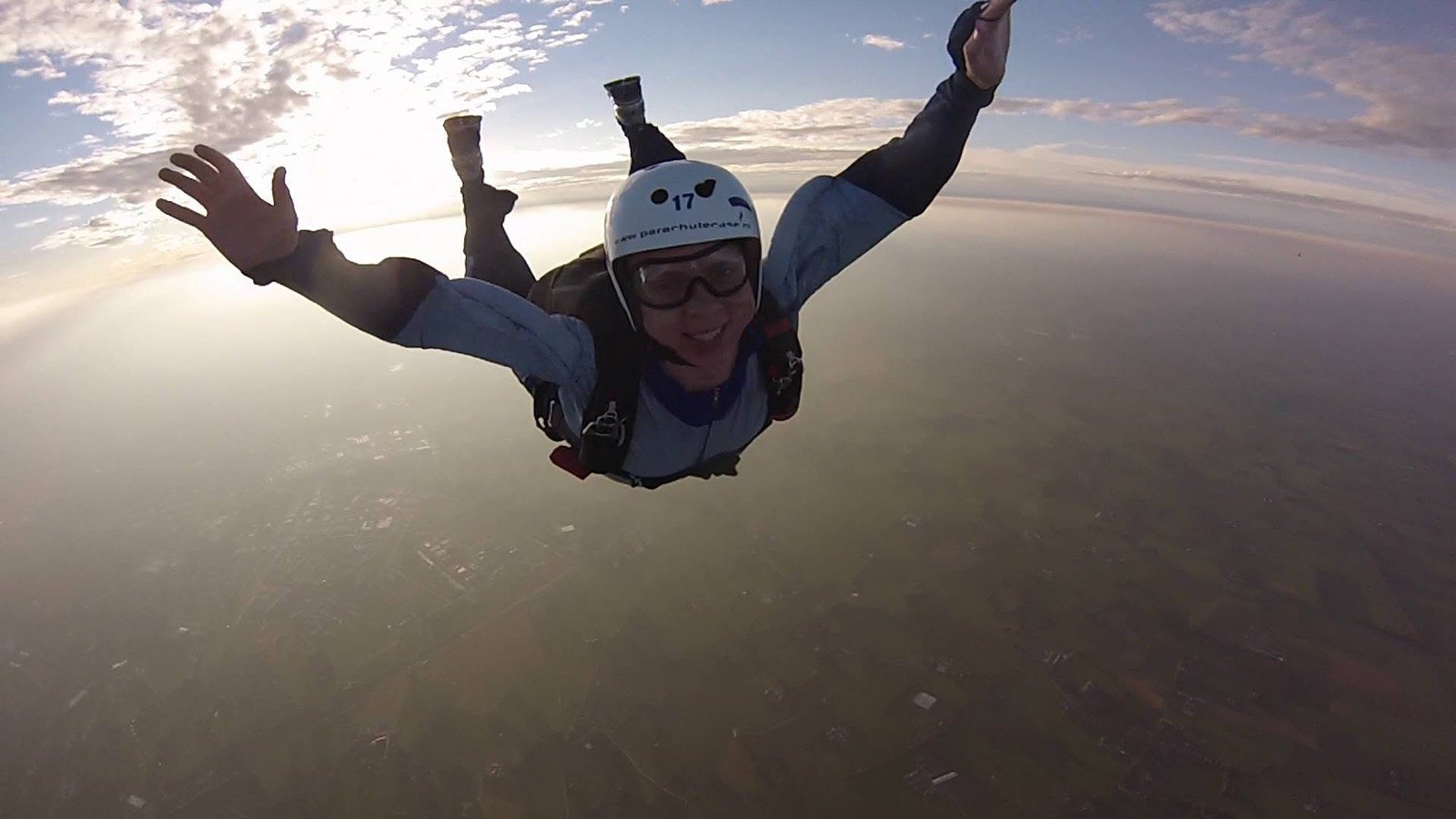 Peter skydiving in freefall, arms spread, over the Dutch countryside.