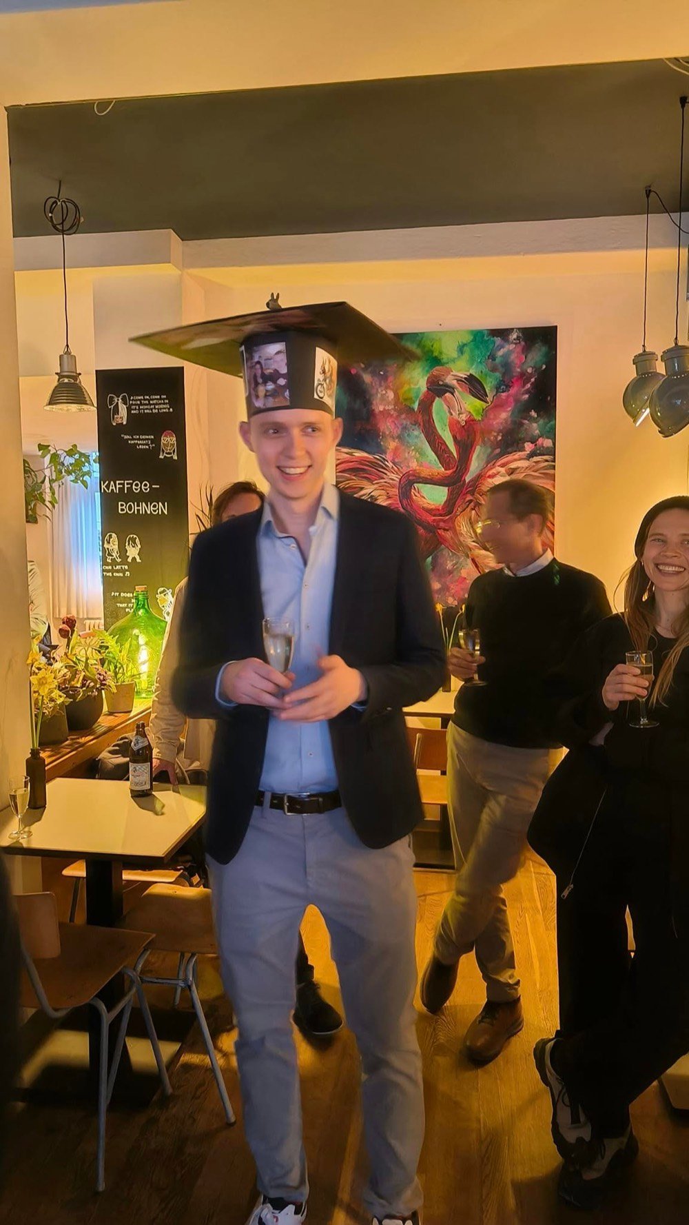Peter in a decorated doctoral hat, holding a glass of champagne at his PhD graduation celebration.