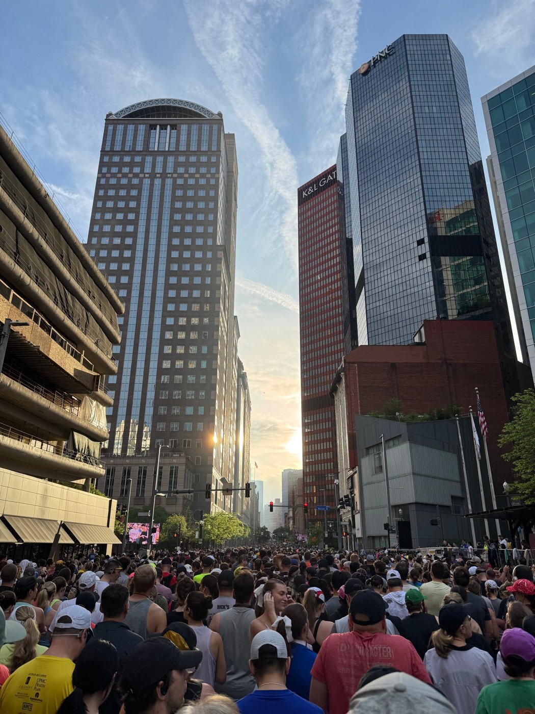 A crowd of runners filling a downtown Pittsburgh street at sunrise for a road race.